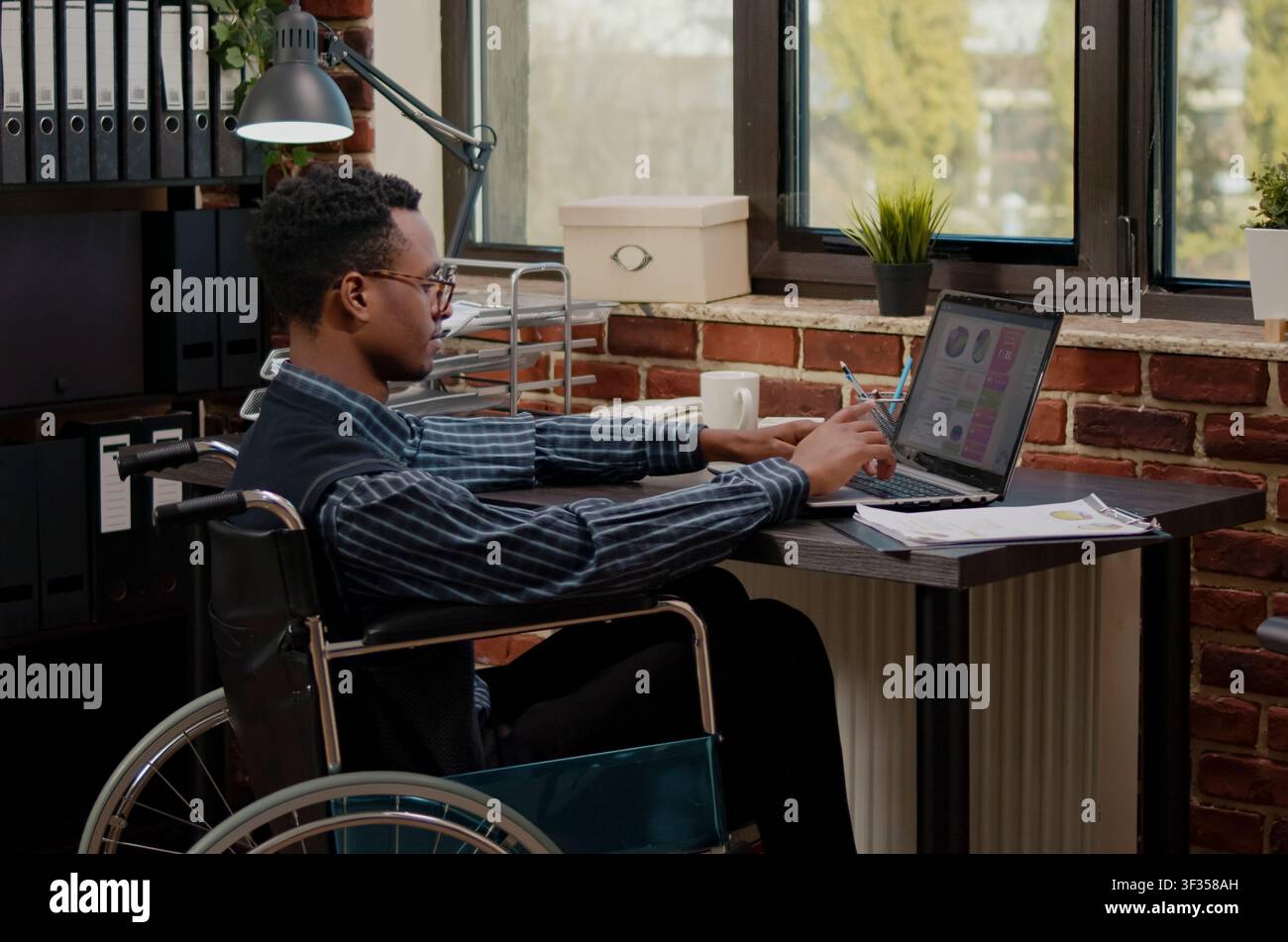 Wheelchair worker plans business growth online at a workplace computer while creating software, writing algorithms and supporting cloud computing development in an IT office. Stock Photo