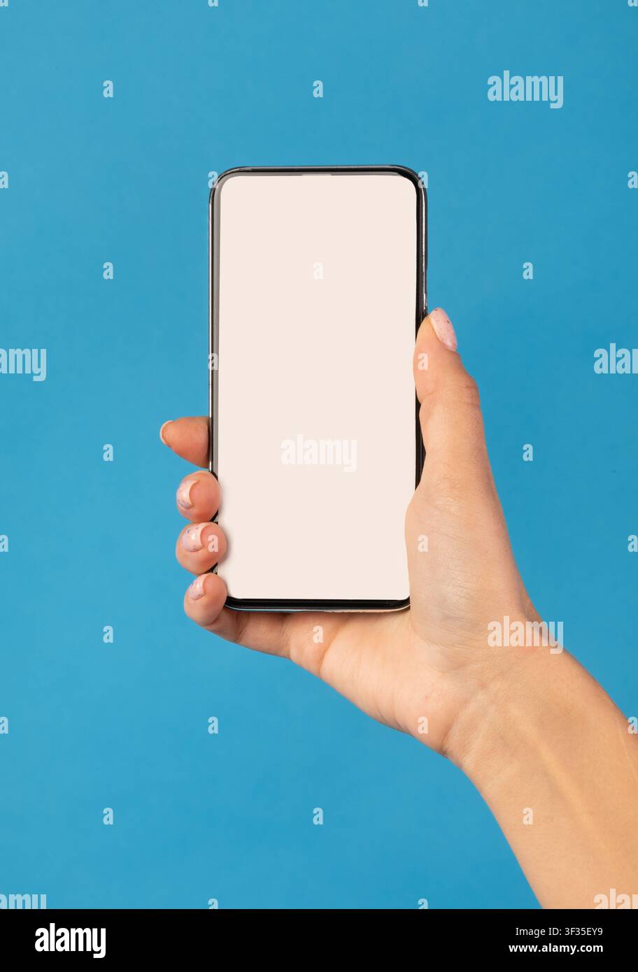 Female Hand Holding Phone With White Screen Over Blue Background Stock Photo