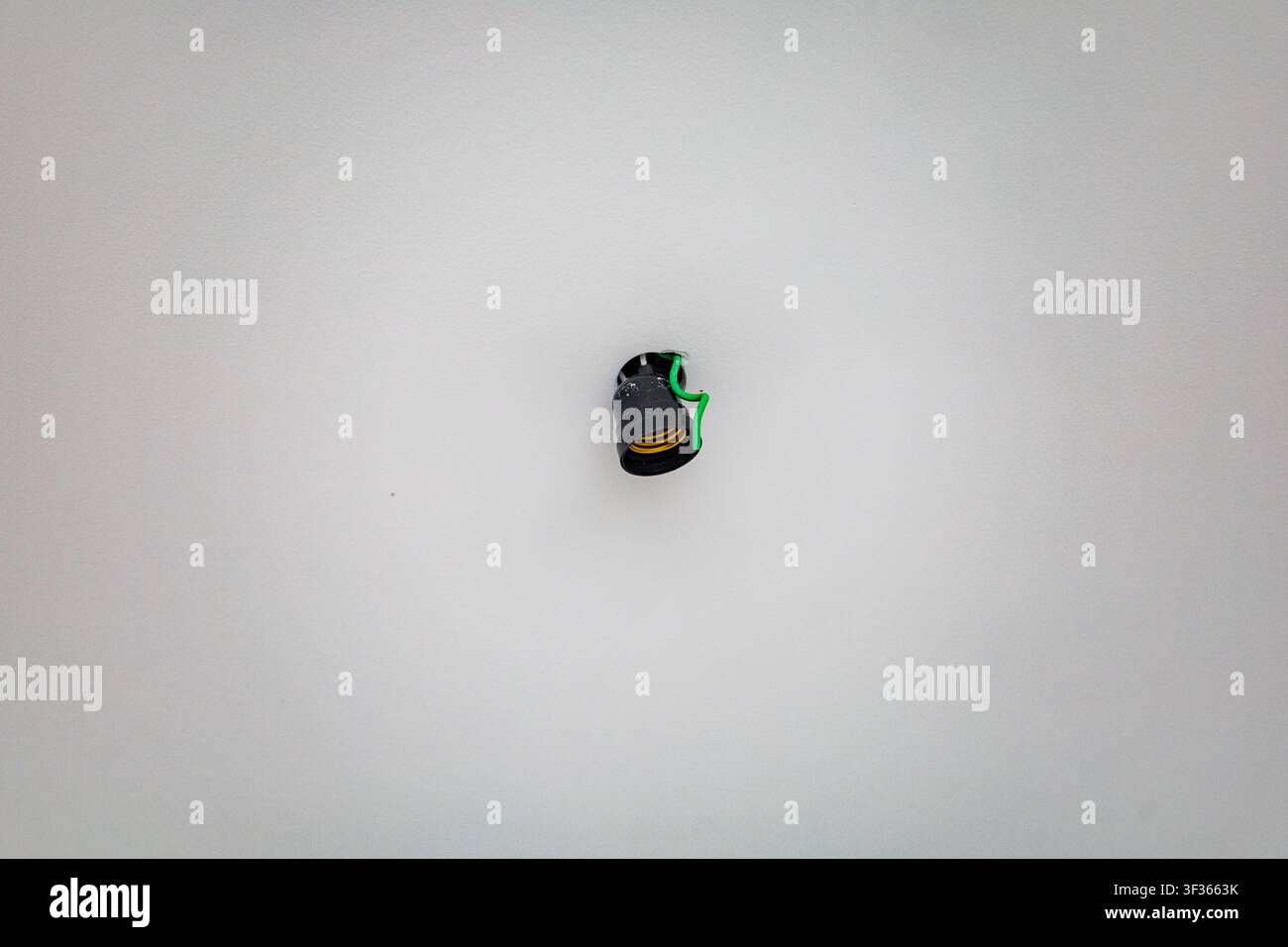 Unfinished electrical installation featuring a black light socket on a white ceiling surface Stock Photo