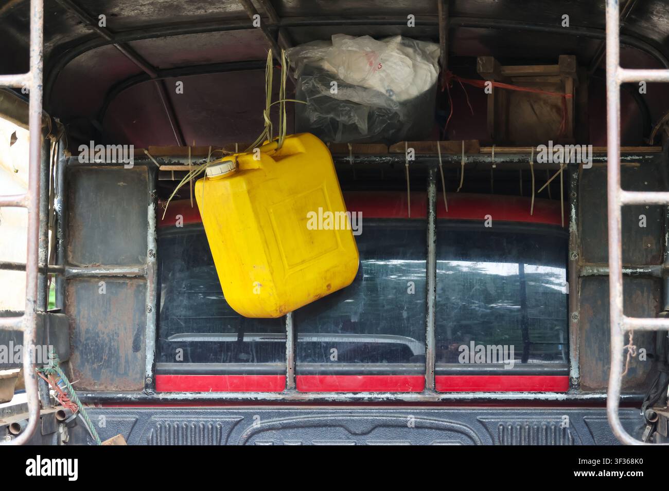 A yellow plastic jerrycan hanging from rear of old pickup truck, weathered metal frame and packed cargo create gritty utilitarian scene with rustic te Stock Photo