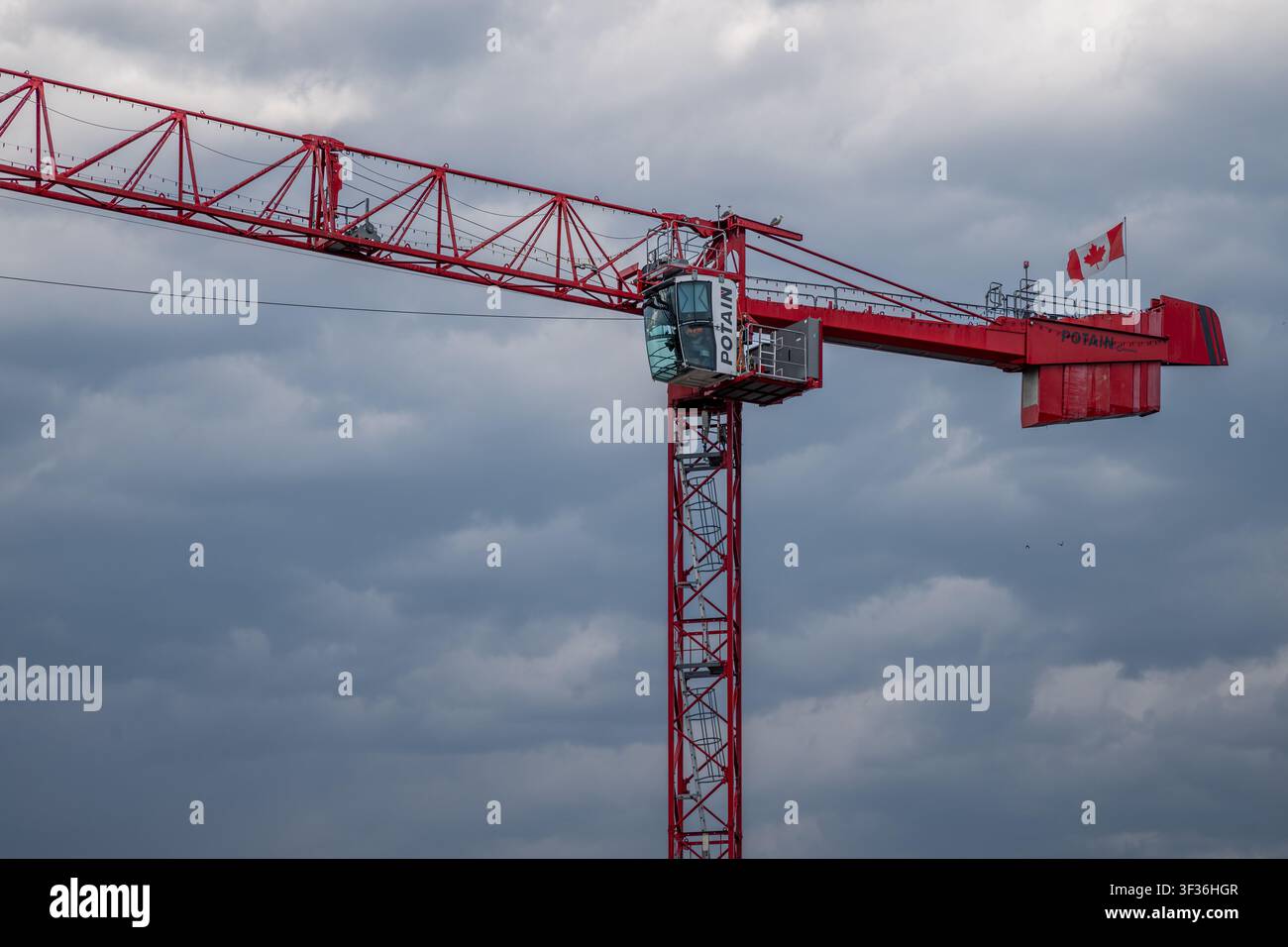 Red Potain tower crane featuring a flying Canadian flag against a cloudy overcast sky in Vancouver, British Columbia. Stock Photo