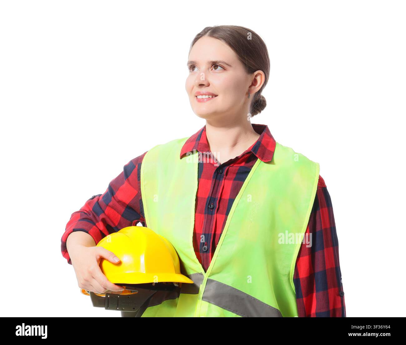Smiling female construction worker in a safety vest holding a yellow hard hat, looking up with a thoughtful expression Stock Photo