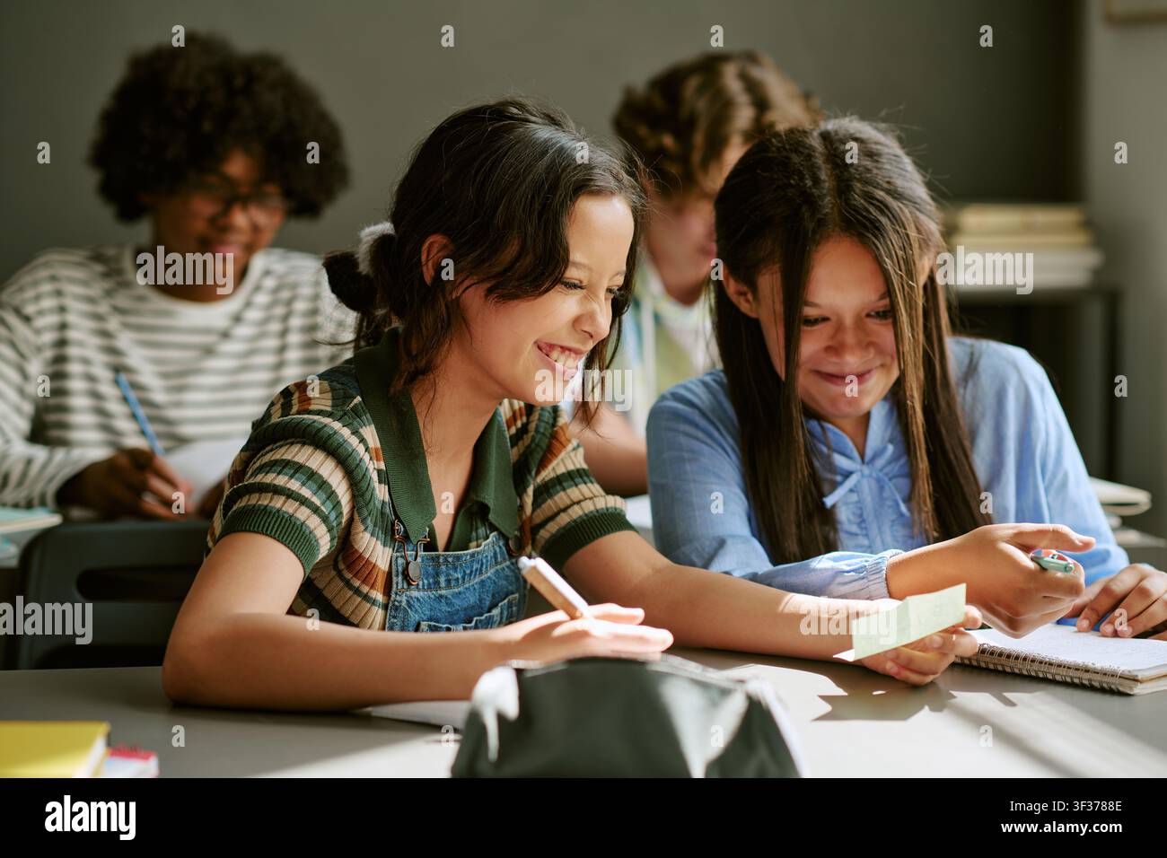 Diverse Teen Girls Smiling while Reading Notes during Classwork Stock Photo
