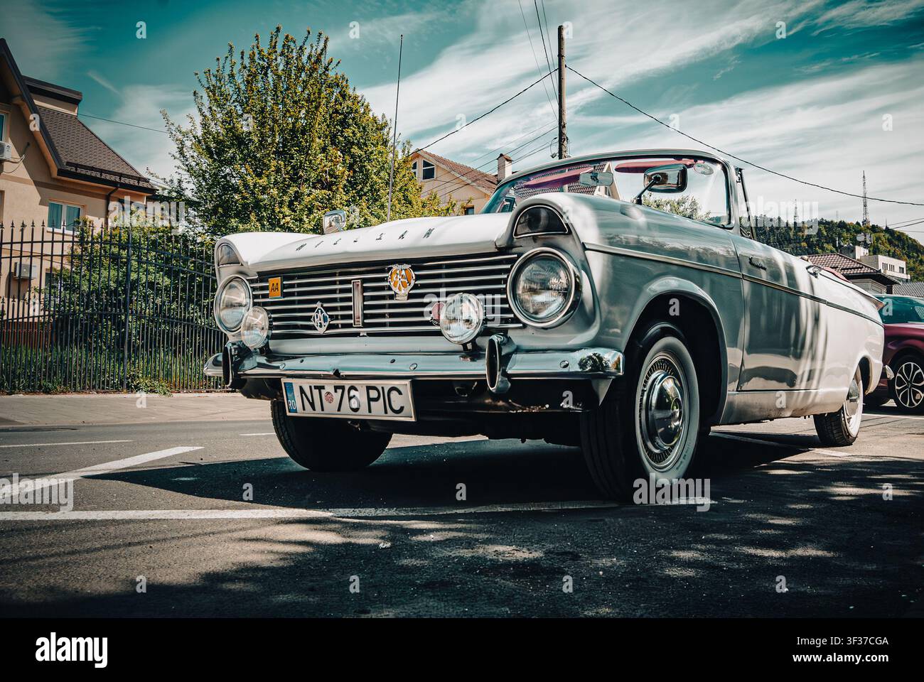 Vintage white Hillman convertible automobile parked on a sunny city street, featuring a chrome grille adorned with classic badges and whitewall tires Stock Photo