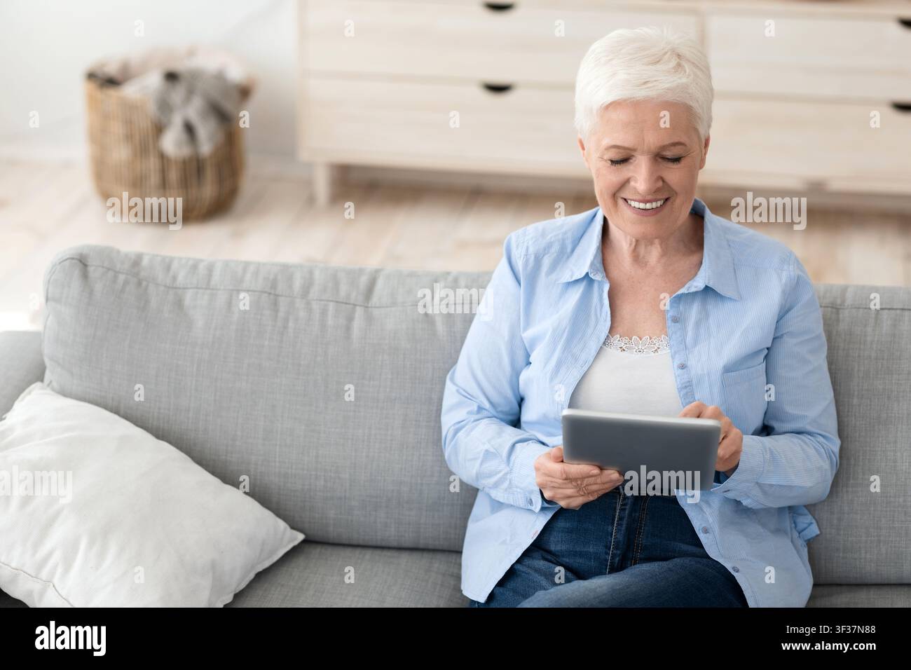 Charming elderly lady sitting on couch at home using digital tablet computer Stock Photo