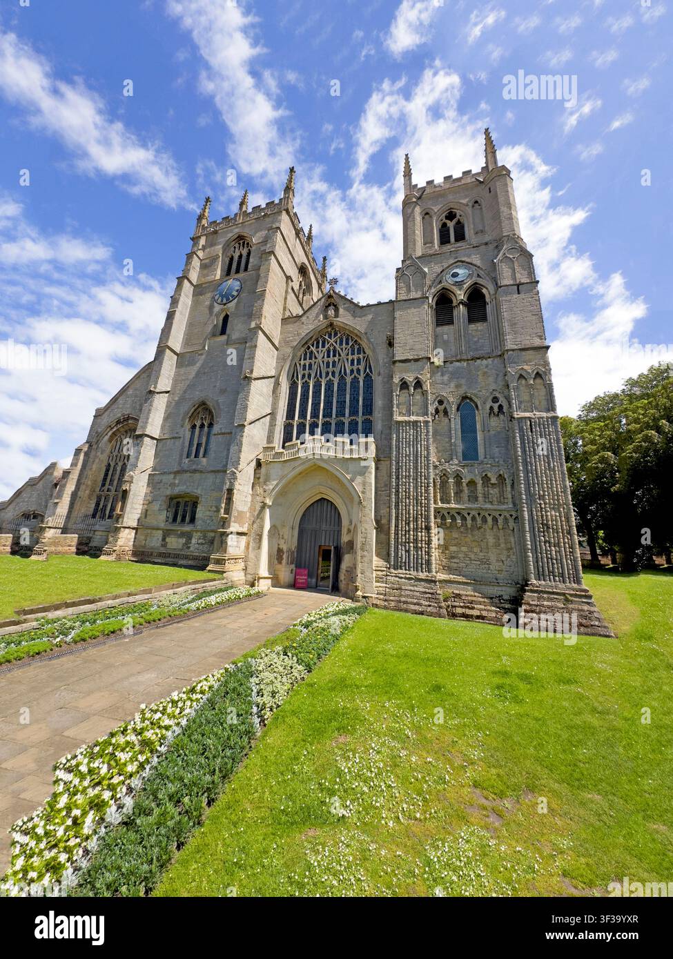 Unique low-angle summer sunny view of King's Lynn Minster, showing its twin west towers, large traceried window and medieval stone frontage. Stock Photo