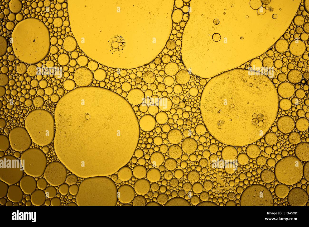Oil and water mixing, forming abstract golden bubbles and patterns on a liquid surface Stock Photo