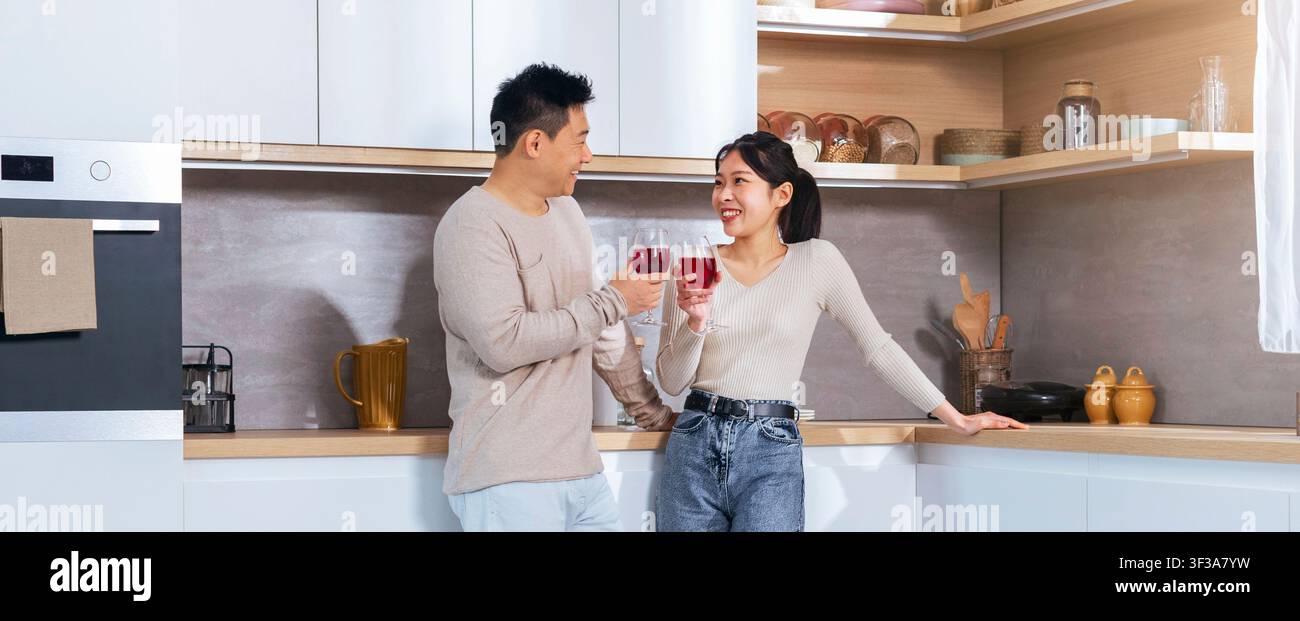 Happy Asian Couple Toasting Drinks In Modern Kitchen, Celebrating Special Moment Together Stock Photo