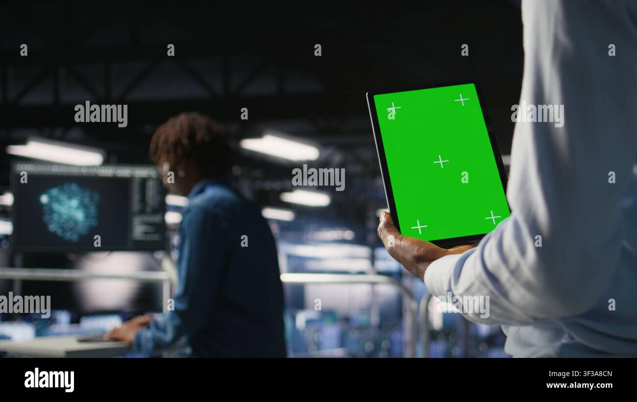Data center worker using green screen mockup tablet, doing maintenance on rigs handling AI tasks. Server hub admin using chroma key device to manage storage arrays supporting deep learning, Stock Photo