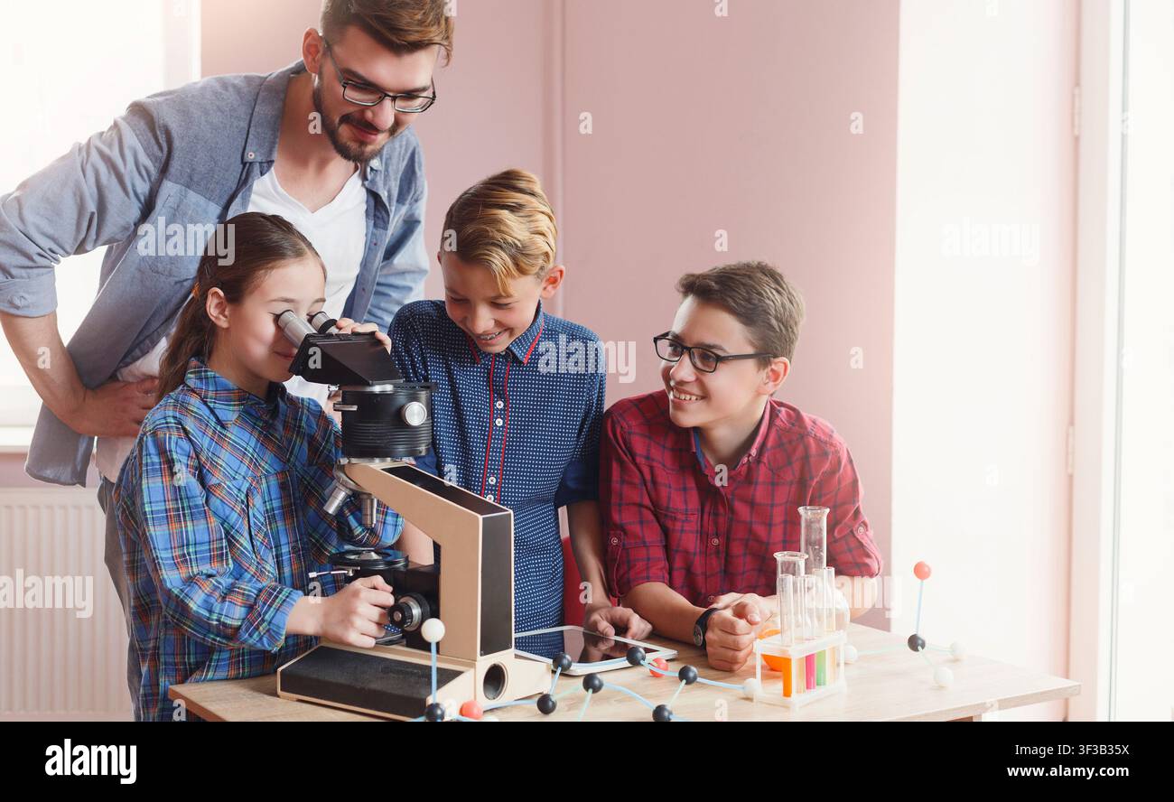 Children engaged in hands-on science experiment with microscope in classroom Stock Photo