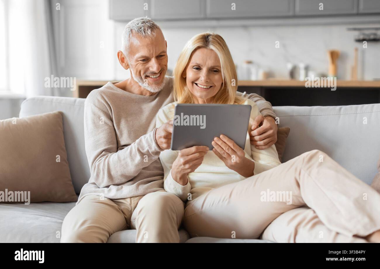 Excited smiling senior spouses using digital tablet computer at home Stock Photo