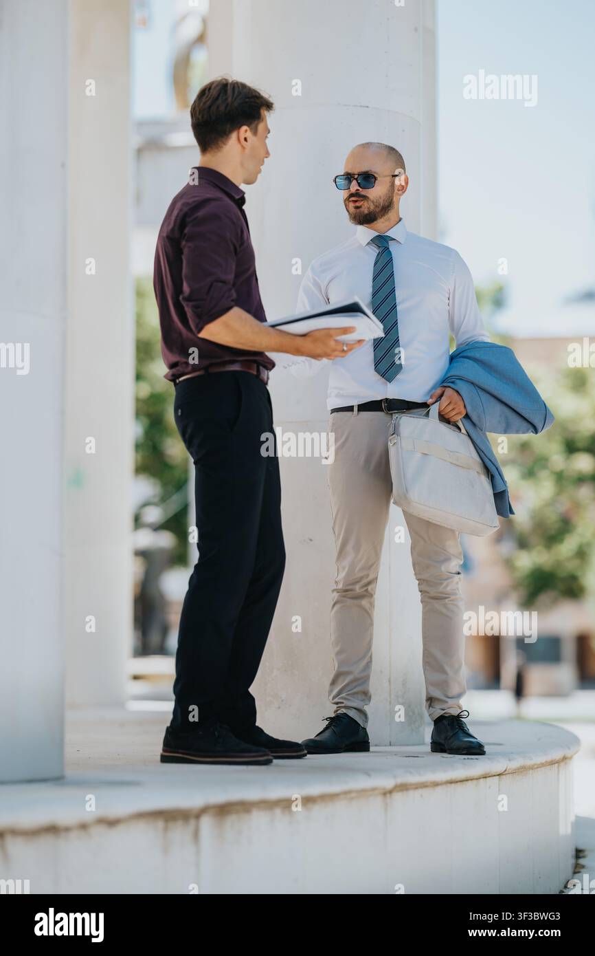 Two businessmen discussing documents while standing outside a modern office building Stock Photo