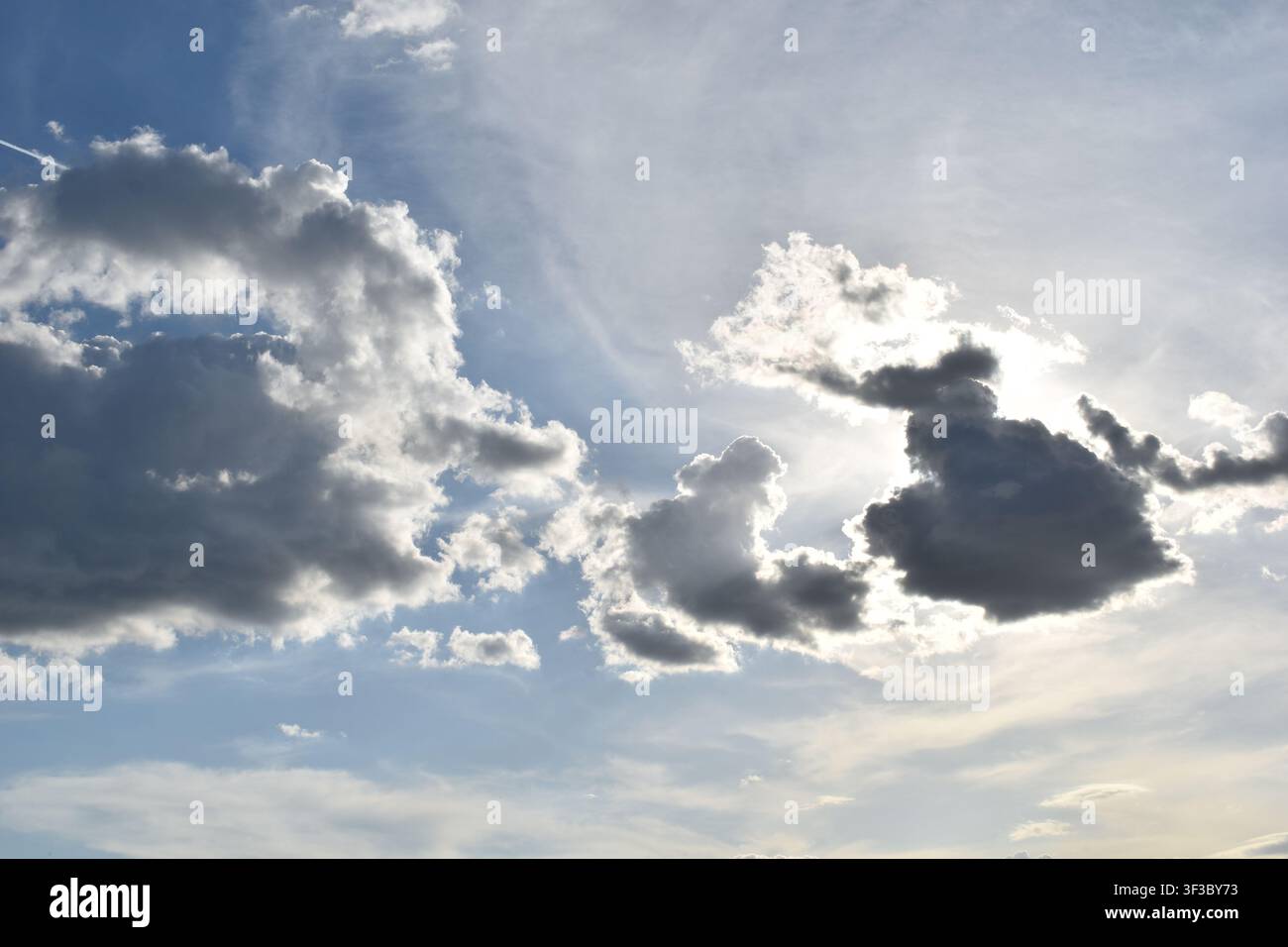Dramatic dark clouds with sun shining from behind against a blue sky Stock Photo