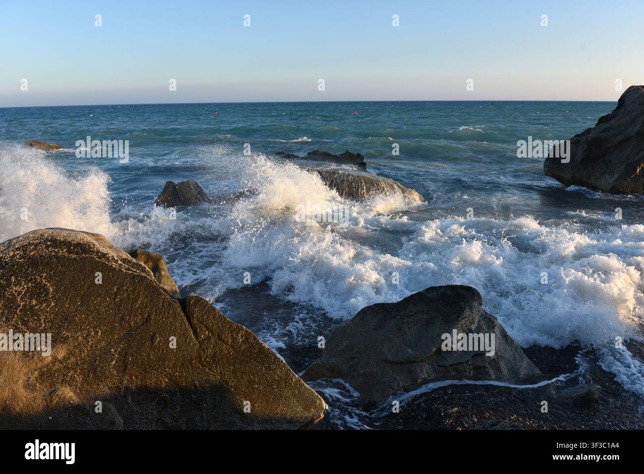 Sea stack on a pebble shore with incoming waves at sunset in Cyprus Stock Photo