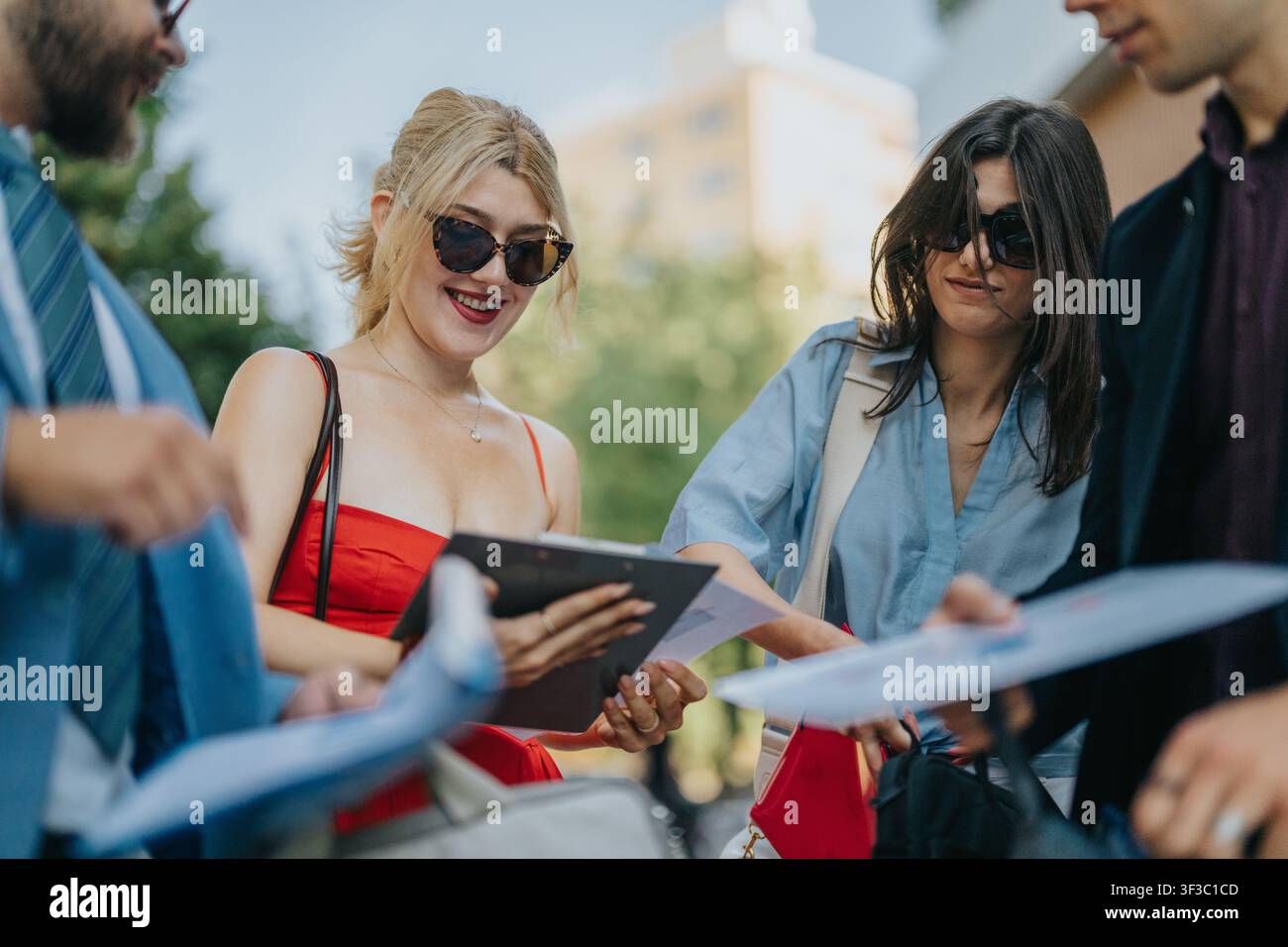 Young friends collaborating outdoors in the city, smiling and sharing documents and a tablet Stock Photo