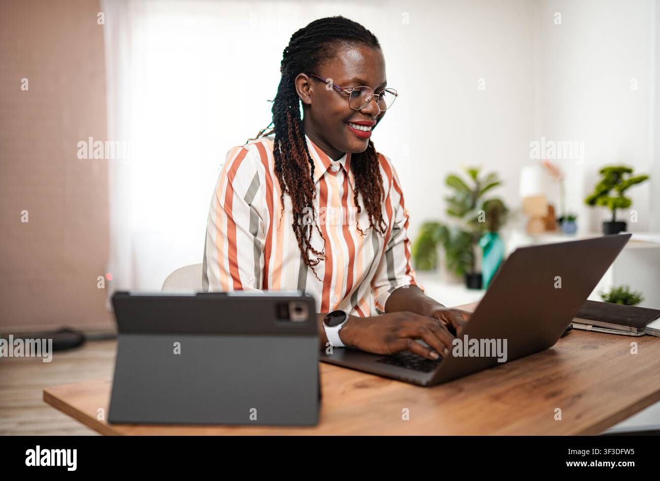 Young Black woman smiling, working on laptop in home office Stock Photo