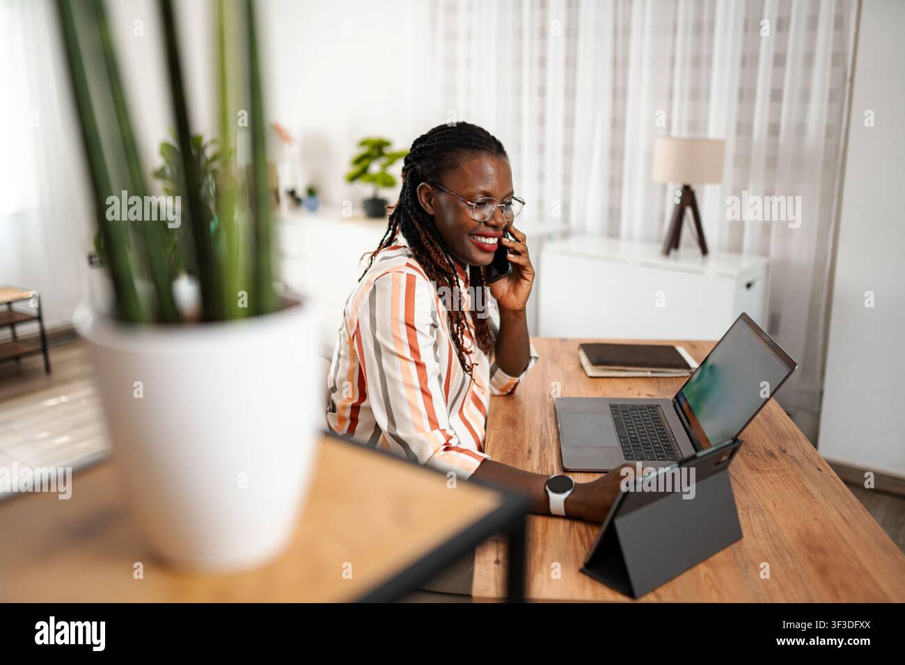 Smiling black woman talking on phone working from home Stock Photo