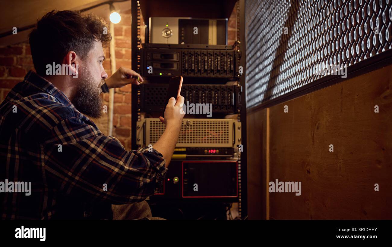 Male technician verifying server rack status with mobile device in technical room Stock Photo