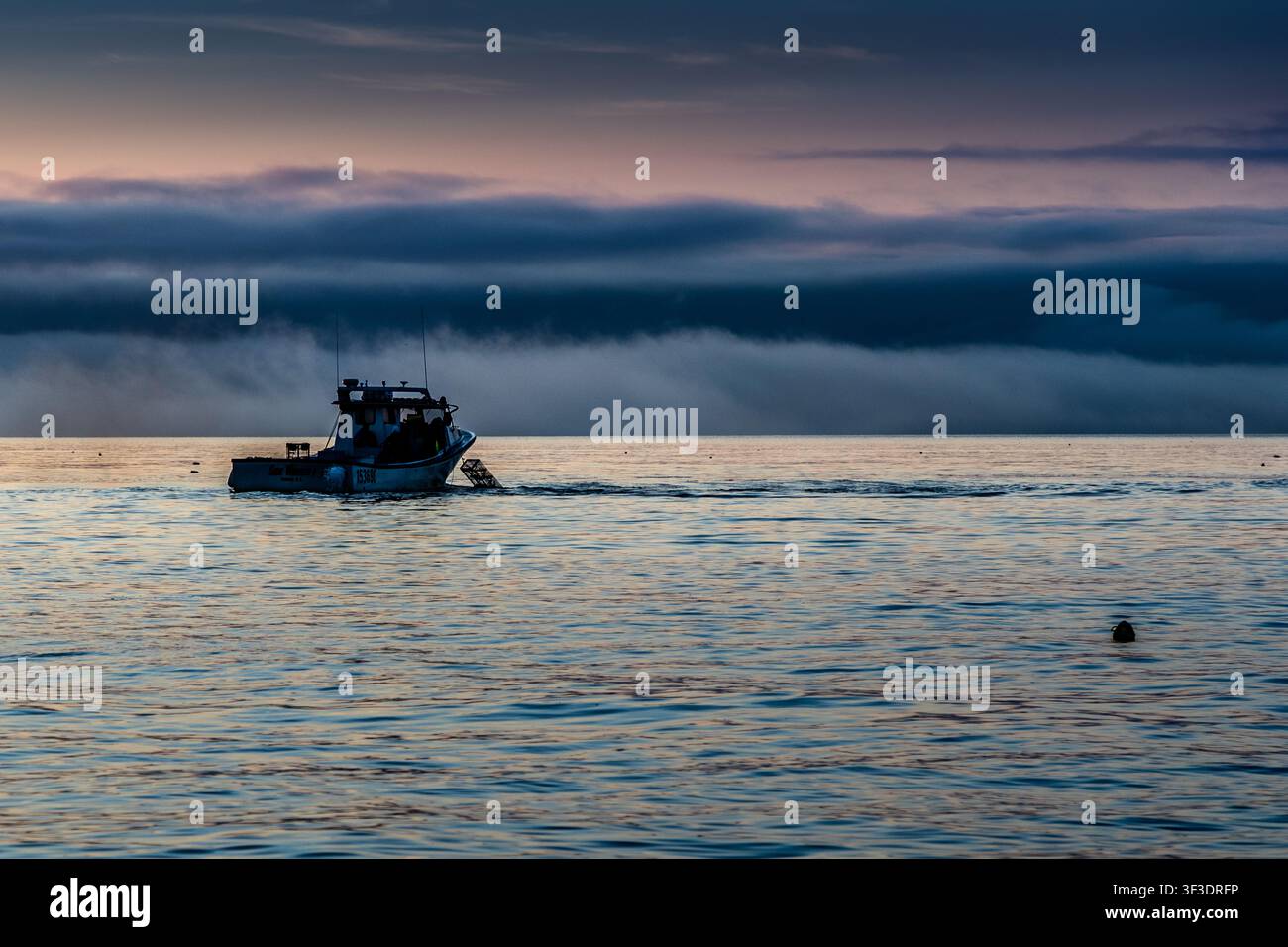 At dawn, a lobster boat navigates through a low bank of fog on St Ann’s Bay near Indian Brook, Nova Scotia, Canada Stock Photo