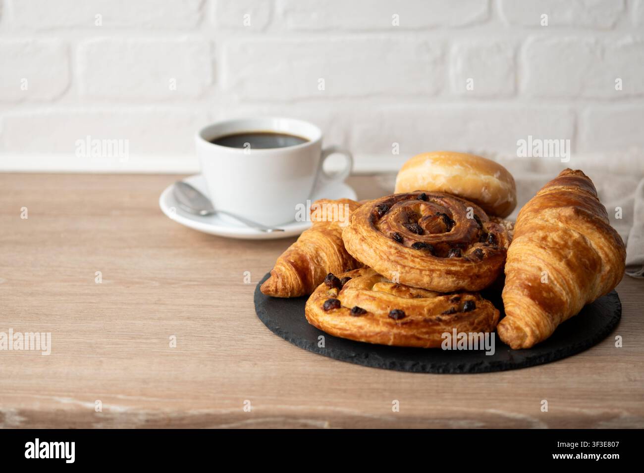 Assorted breakfast pastries with black coffee on wooden table Stock Photo