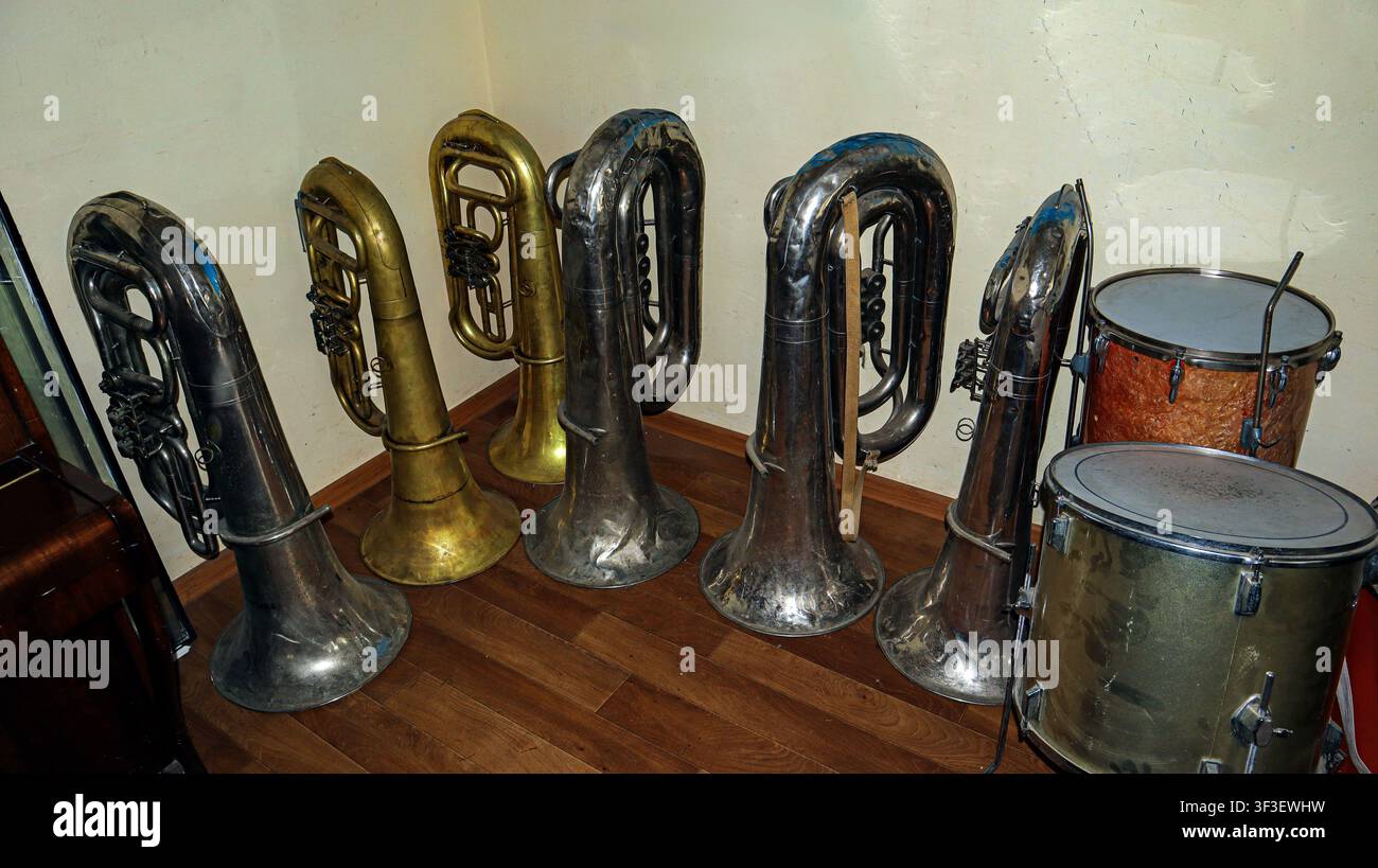 Old brass instruments, including tubas and a drum, are neatly arranged in a music school storage room, showcasing the history of musical education. Stock Photo