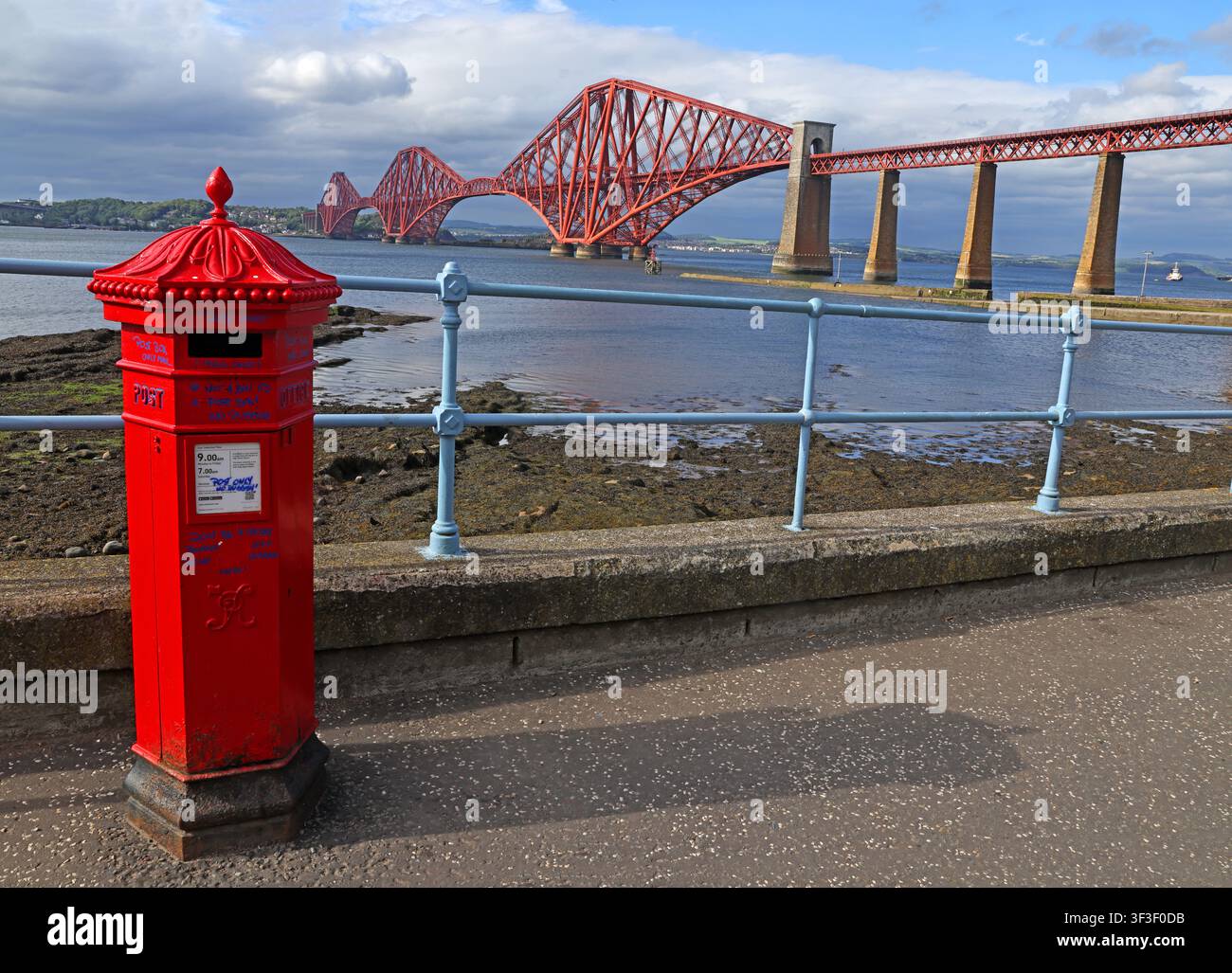 Iconic Victorian-style red post box and the UNESCO-listed Forth railway Bridge on the waterfront at South Queensferry, Scotland., EH30 9HN Stock Photo