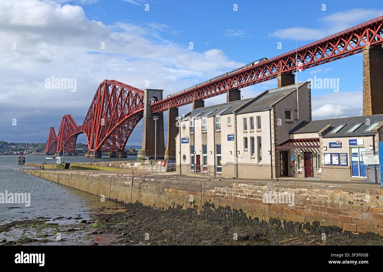 A ScotRail Aberdeen service crosses the Forth Railway Bridge above Hawes Pier and the RNLI lifeboat station at South Queensferry., EH30 9HN Stock Photo