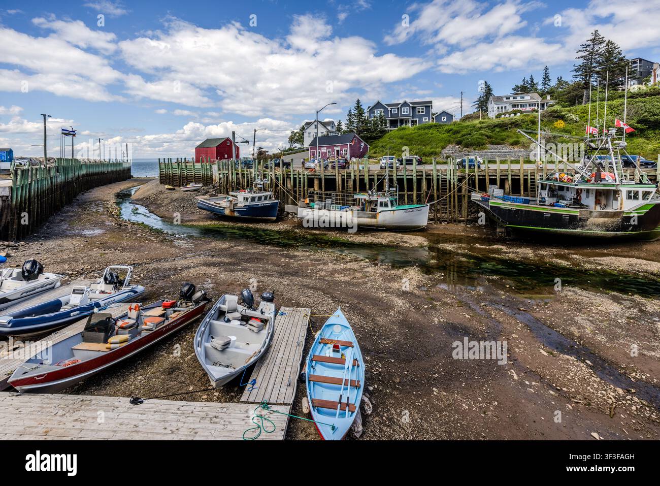 Fishing boats lie close together on the mudflats of Halls Harbour, which have been exposed at low tide, on the Bay of Fundy, Nova Scotia, Canada. Red-painted huts line the wooden quay above the jetty Stock Photo