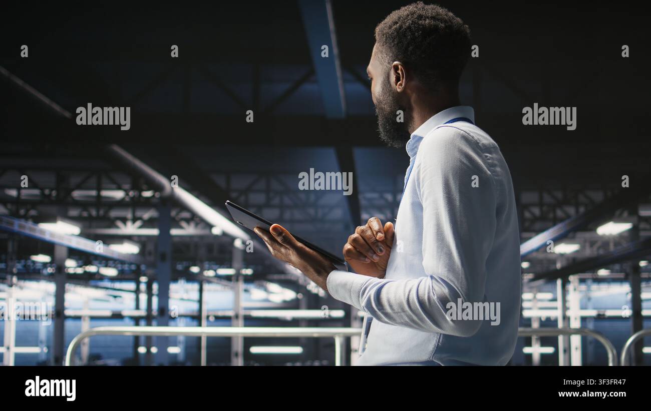 Engineer walking on data center industrial platform, performing system maintenance. IT professional using tablet to do upgrades, resolving bugs and enhancing infrastructure stability, Stock Photo