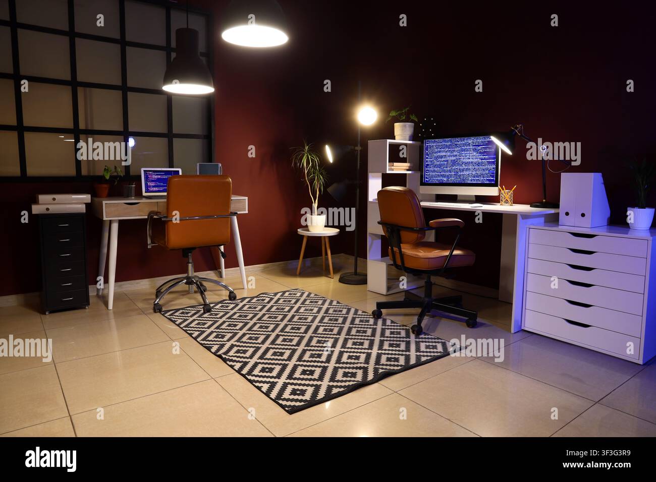 Modern home office interior with two computer workstations and coding on screens at night Stock Photo