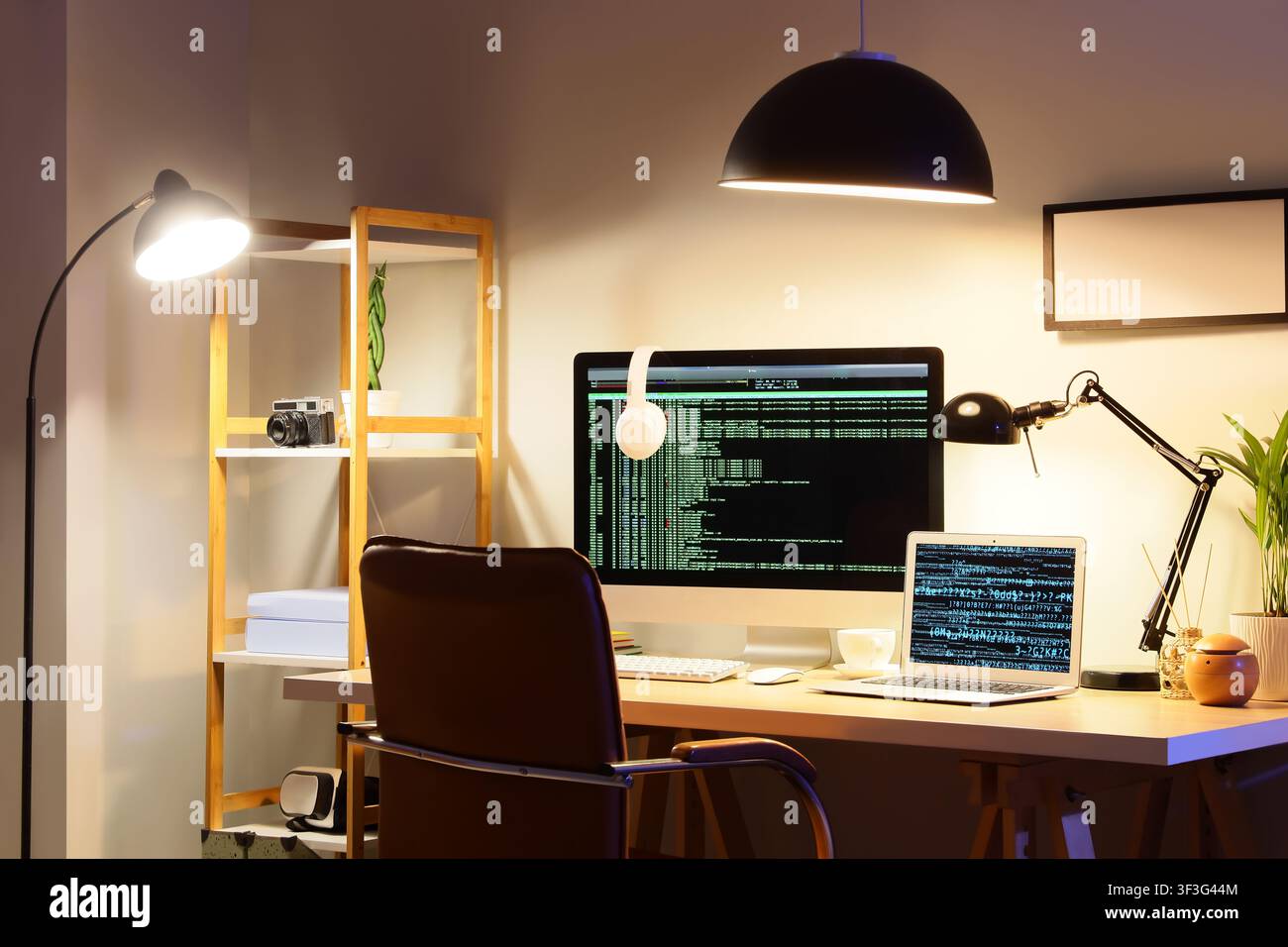 Home office workspace with computer monitor and laptop displaying code at night, remote work and programming Stock Photo