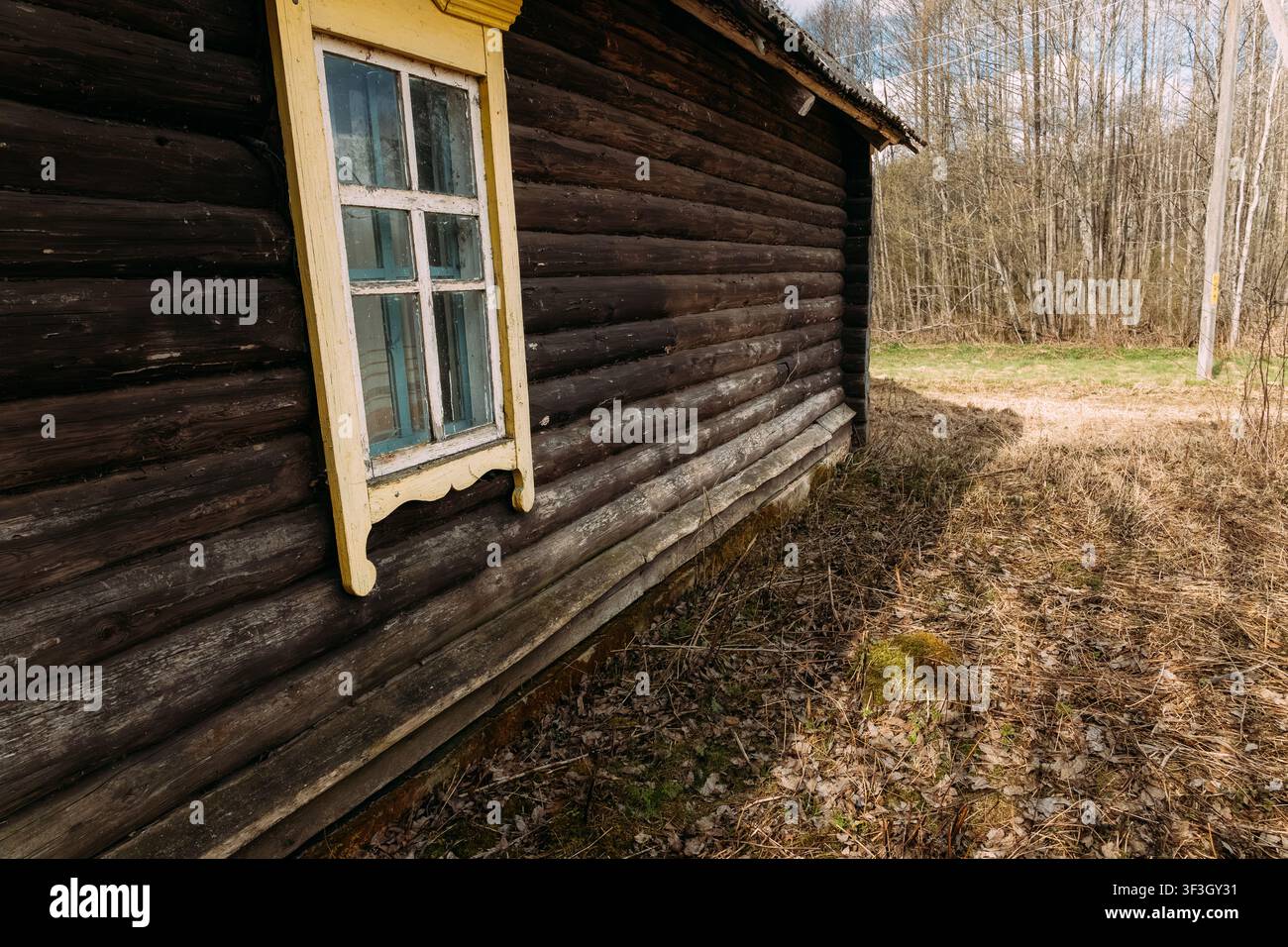 Log wall of an old abandoned house with a yellow window Stock Photo