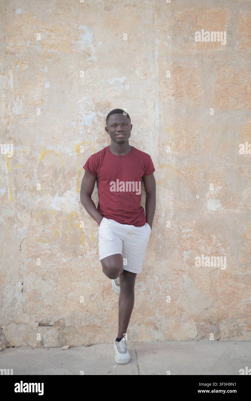 Confident young Black man leaning against a weathered wall Stock Photo
