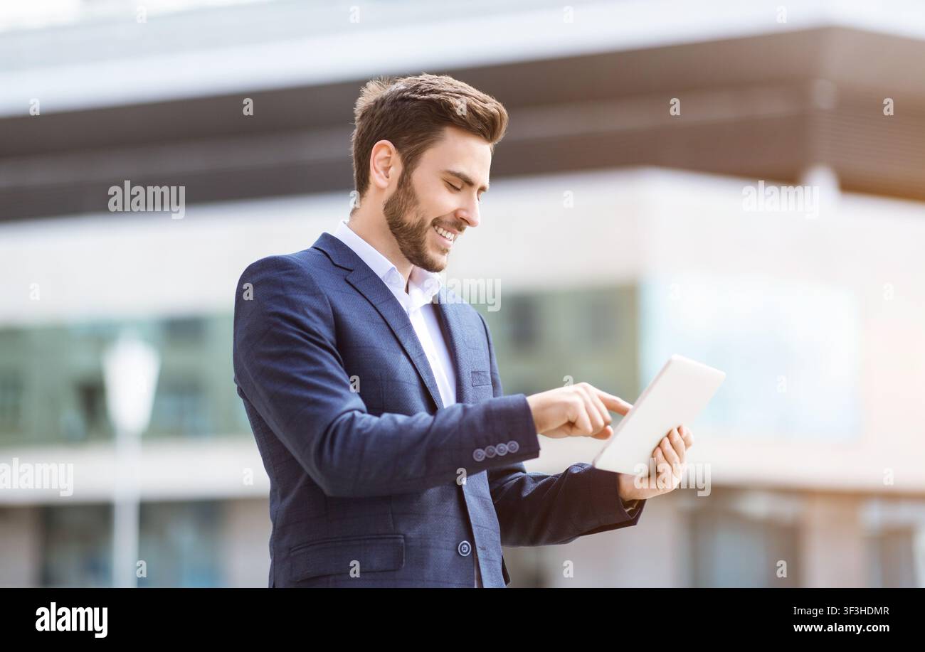Handsome young office worker with tablet computer browsing web on city street Stock Photo
