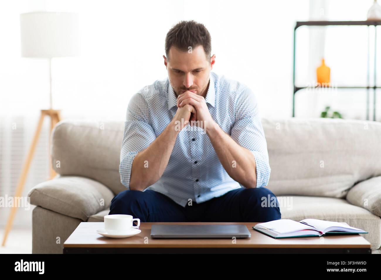 Pensive young guy sitting at table, looking at table Stock Photo