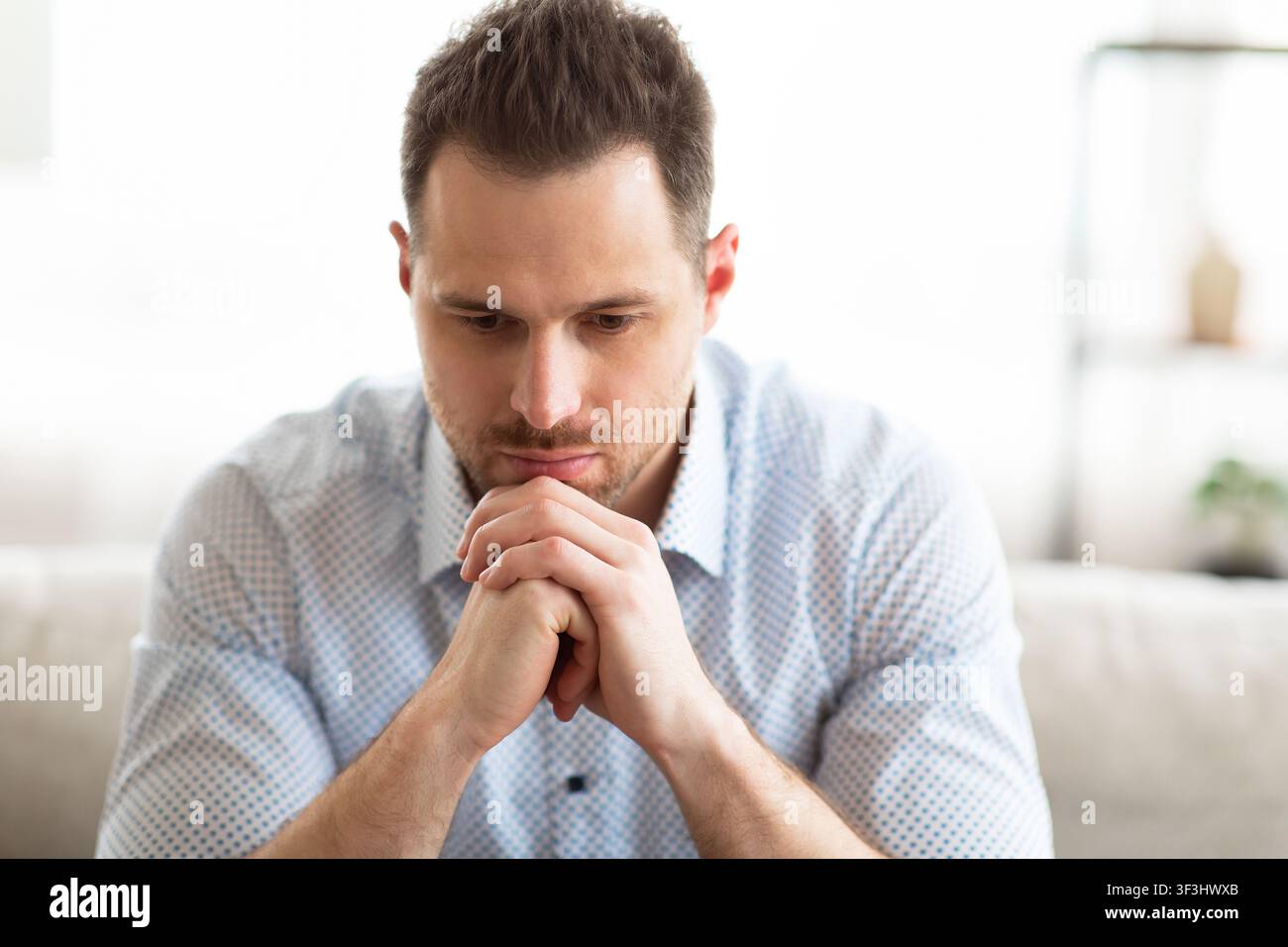 Pensive young guy sitting on couch, looking down Stock Photo