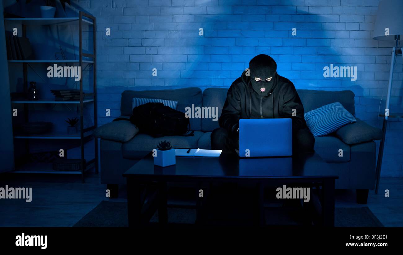 Masked criminal downloading private information using pc Stock Photo