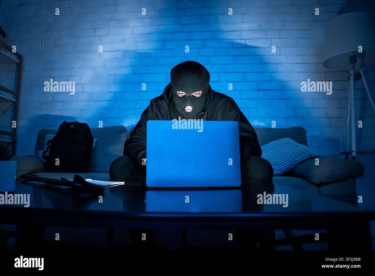 Masked hacker downloading private information using pc Stock Photo