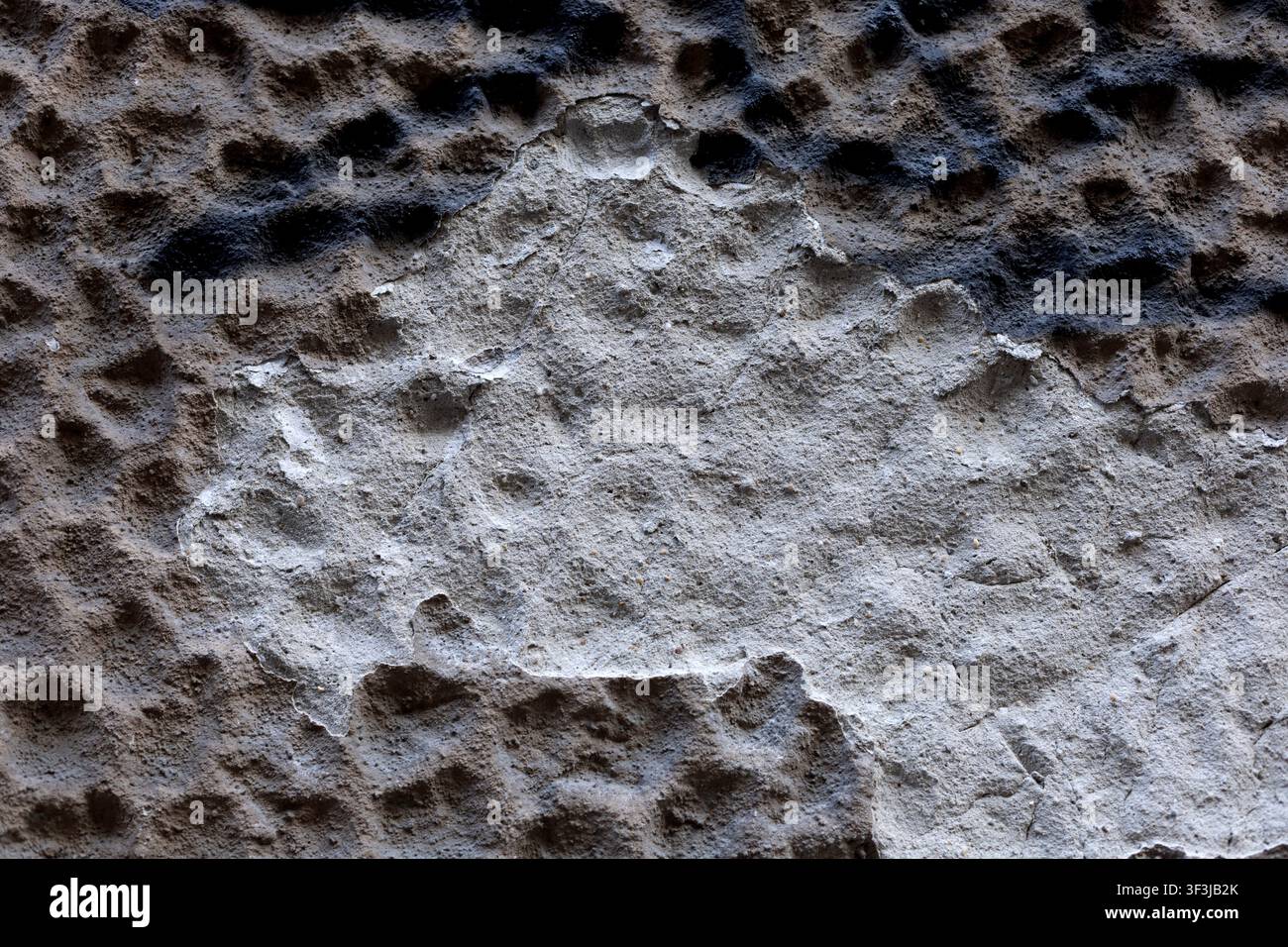 A close-up view of a rough, weathered stone surface with uneven pits and light gray mineral tones. The abstract texture fills the frame and can be use Stock Photo