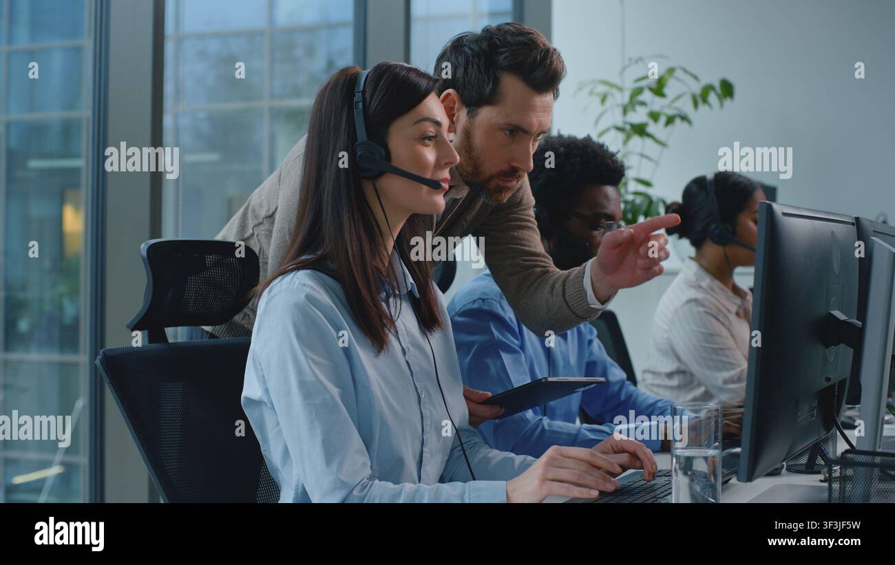Three multiethnic business colleagues operators in call center boss coming checking work talking to woman agent. Multiracial office managers team Stock Photo