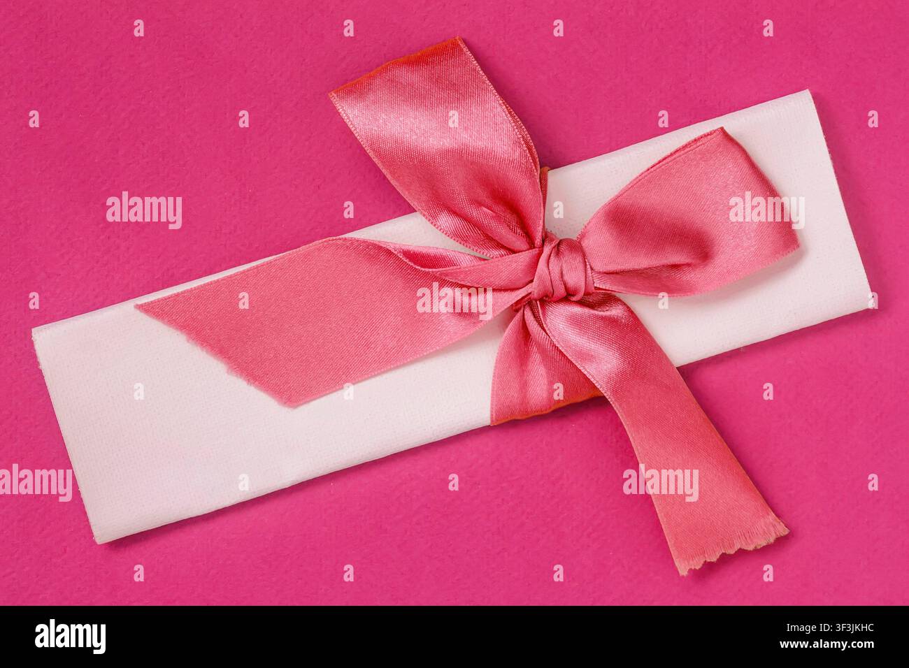 White paper scroll wrapped with glossy pink satin bow on a vivid pink ...