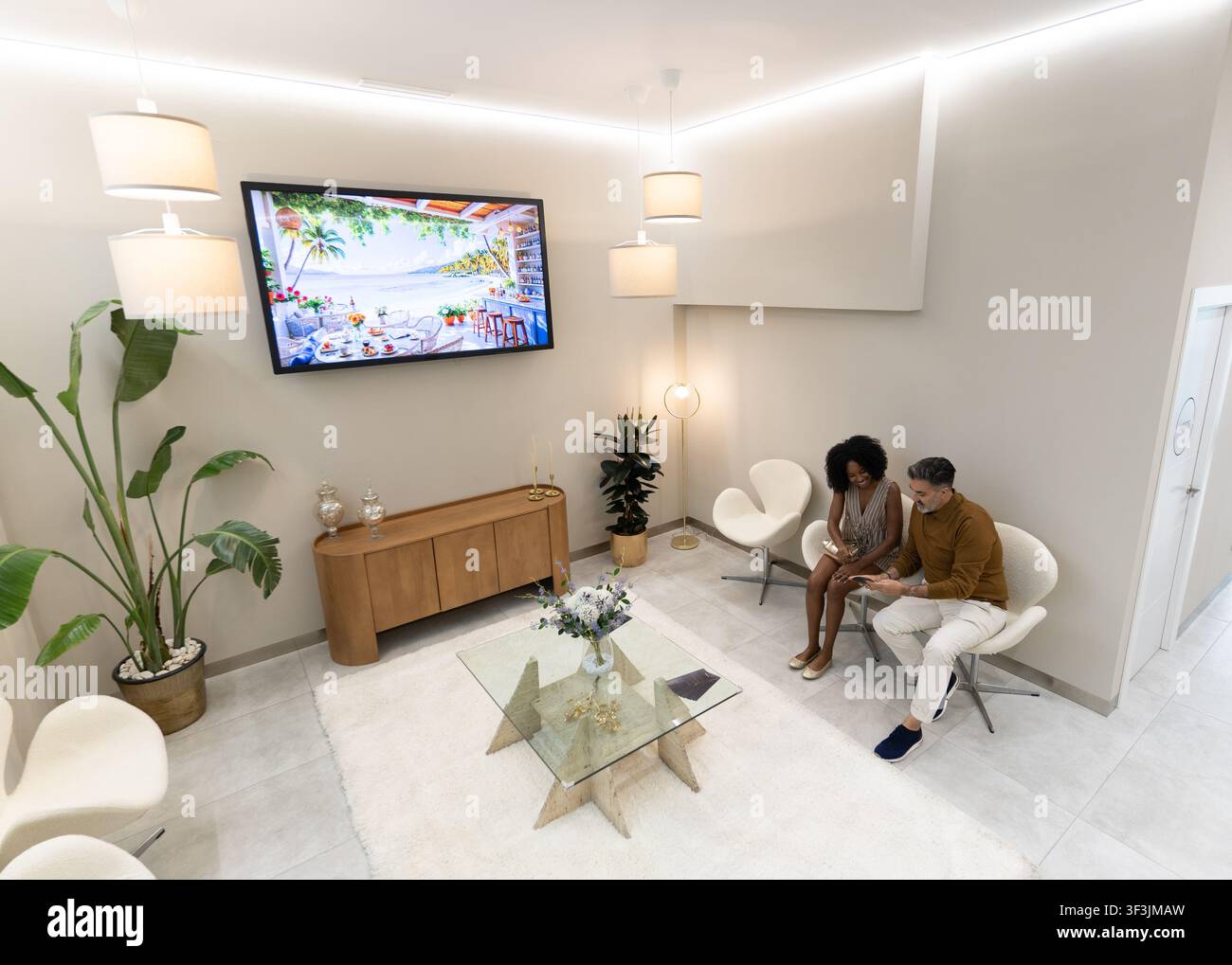 Two diverse people sitting in a professional waiting room, using a digital tablet Stock Photo