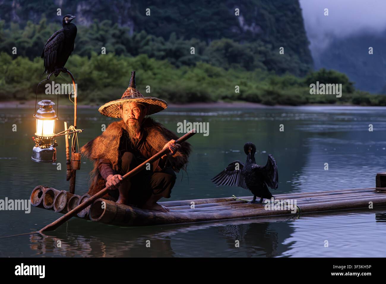 Guilin, Guangxi, China - 18 June 2026: View of a traditional cormorant fisherman on a bamboo raft near Xingpingzhen with a glowing lantern and cormora Stock Photo