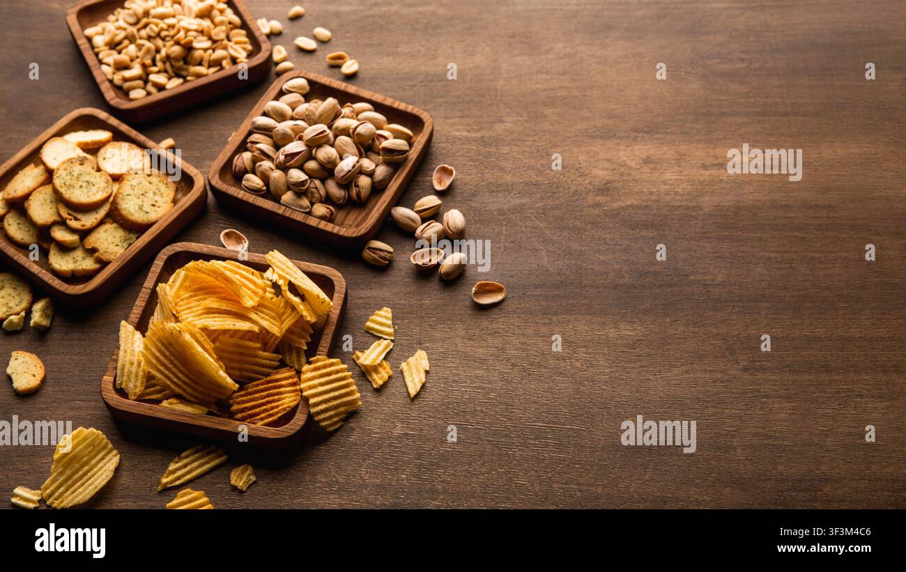Rusks, chips, nuts and pistachios. Snacks in plates on table background Stock Photo