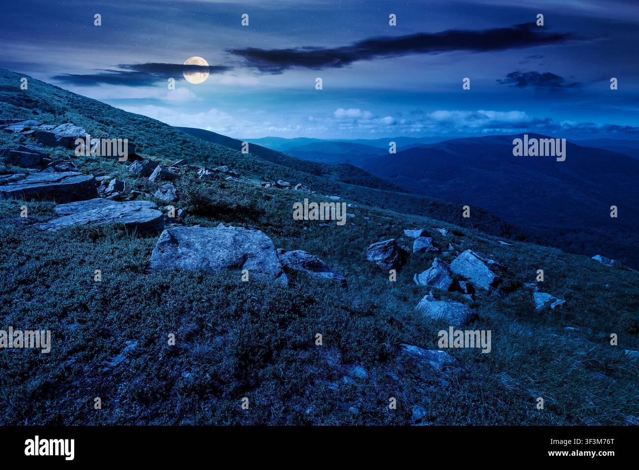 mountain landscape with grass and rock on a slope at night. mysterious view in to the distant valley of carpathian mountains. full moon over mountaino Stock Photo