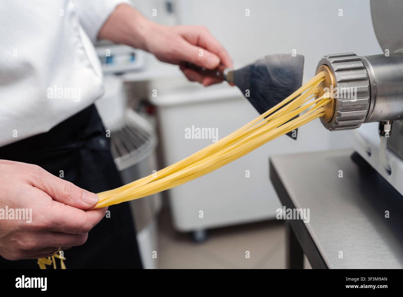 Chef preparing fresh pasta using a machine in a kitchen setting during the day Stock Photo