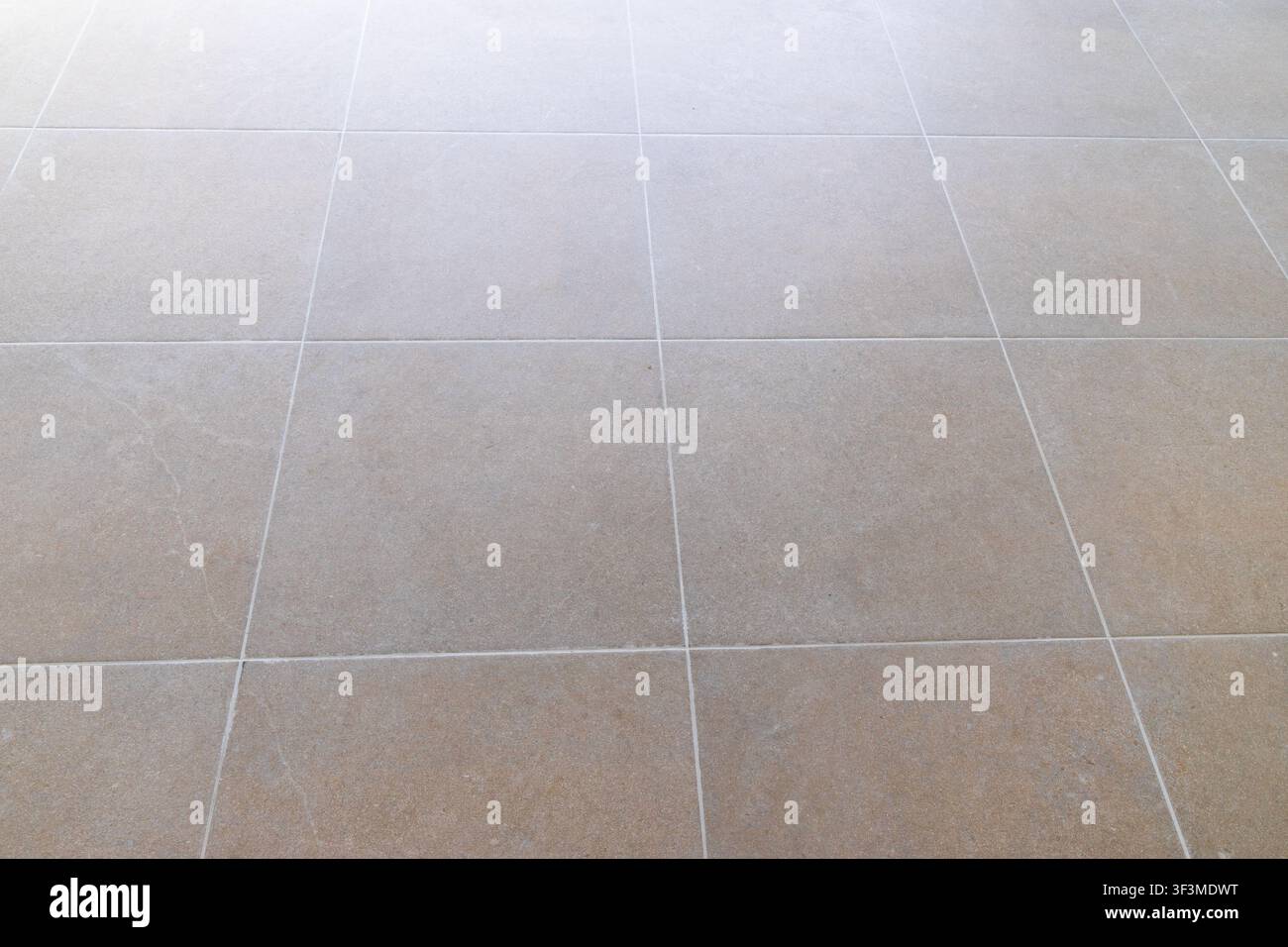 A seamless perspective view of large, square beige floor tiles with fine white grout lines, suggesting a modern and clean interior space Stock Photo