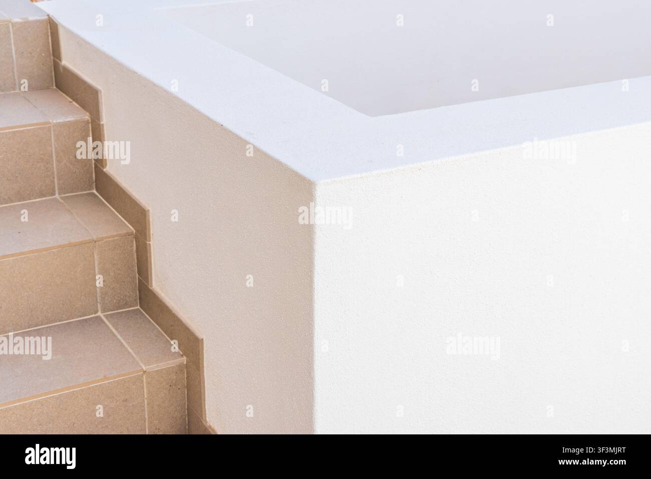 A close-up view showcases the textured surface of a white architectural element adjacent to a set of neutral-toned tiled stairs Stock Photo