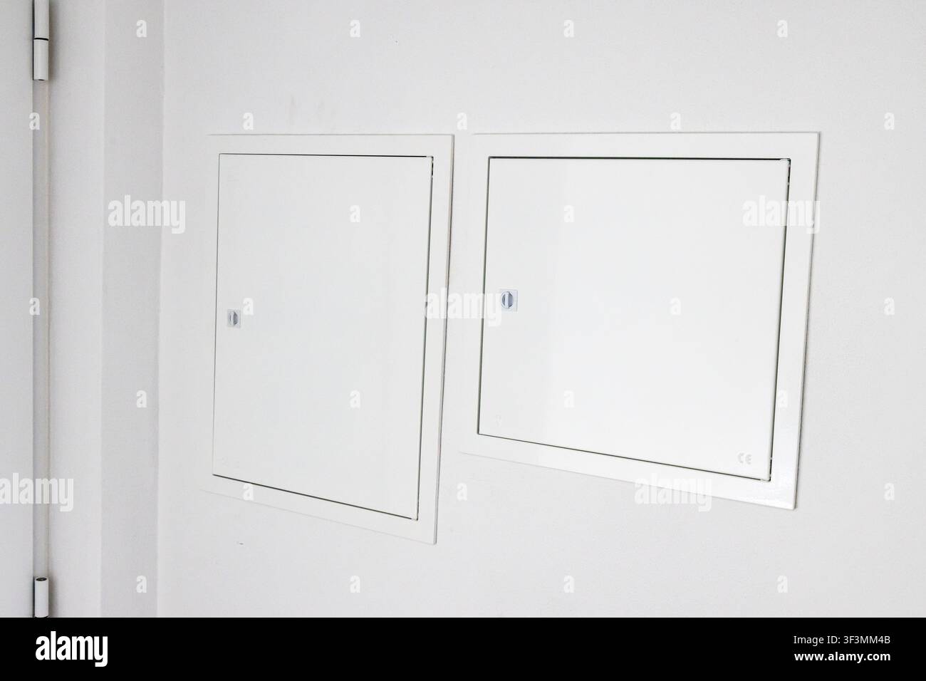 Minimalist interior scene featuring two identical white access panels mounted on a textured white wall, highlighting architectural details Stock Photo