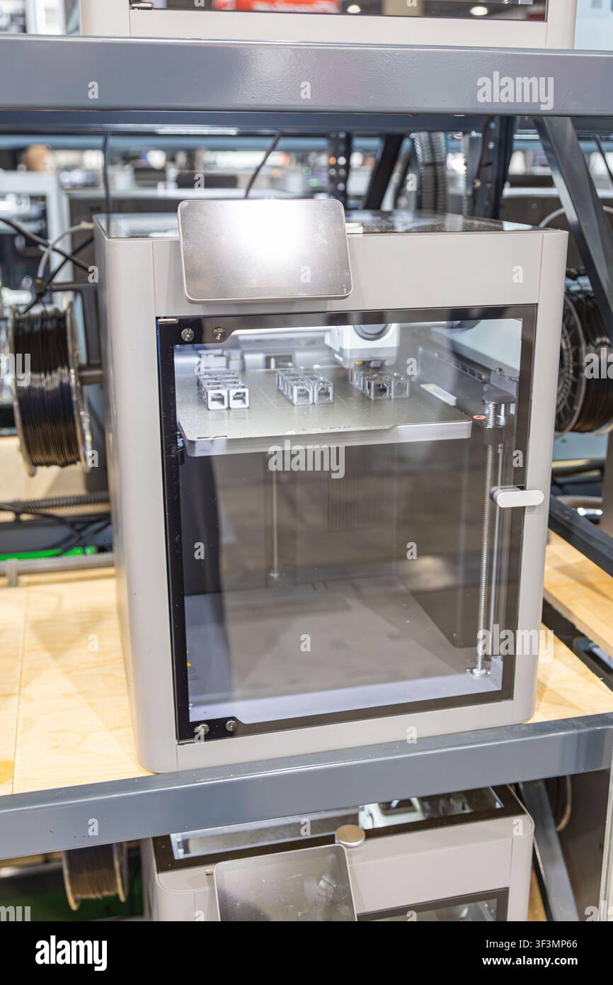 3D printer in industrial workshop, sleek rectangular machine with transparent front panel, metallic finish, control display, printing bed objects, hig Stock Photo